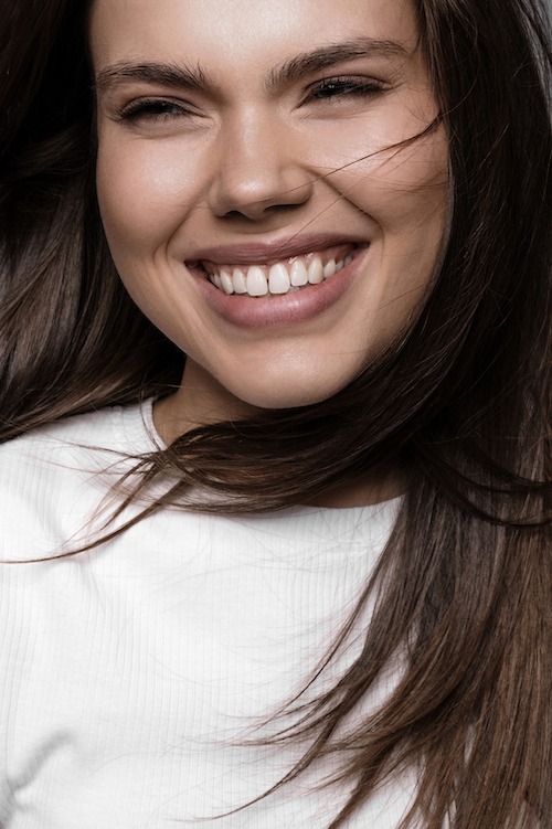 Nahaufnahme einer lachenden jungen Frau mit wehenden braunen Haaren, die Freude und Vitalität ausstrahlt.