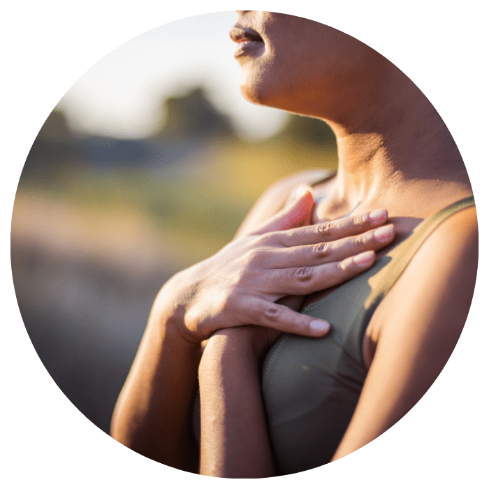 Frau im Freien in meditativer Pose mit Händen auf dem Herzen, symbolisiert Ruhe und Wohlbefinden in einer natürlichen Umgebung.